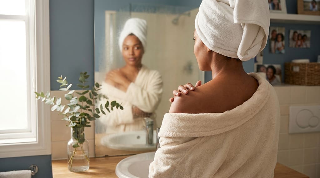 Woman examining her shoulder in a bright bathroom mirror with calm attention